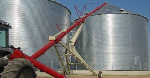 A tractor-driven auger transfers grain from a tray at ground level to the top of a storage bin