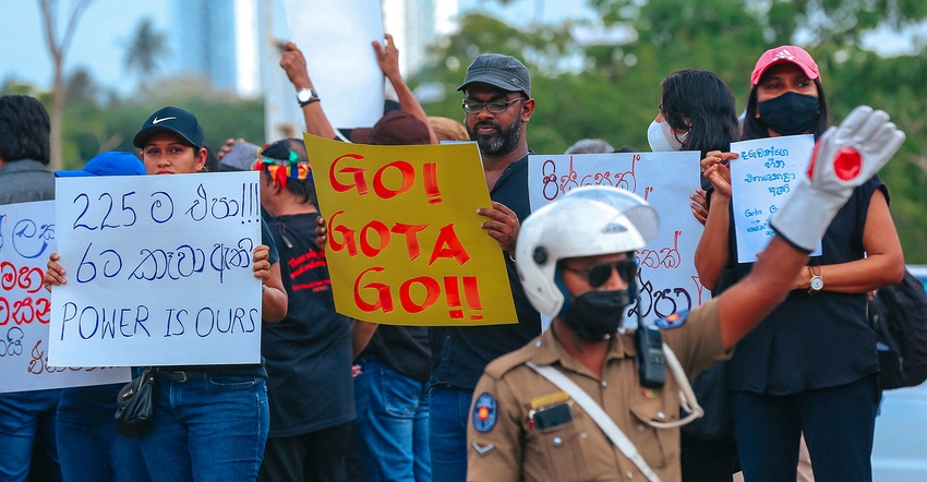 A policeman stands guard as demonstrators (background) take part in a demonstration against the surge in prices and shortage 