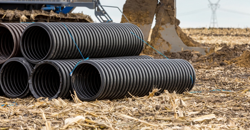 Black corrugated water drainage pipe, field tile, in farm field with tile plow or ditcher in background