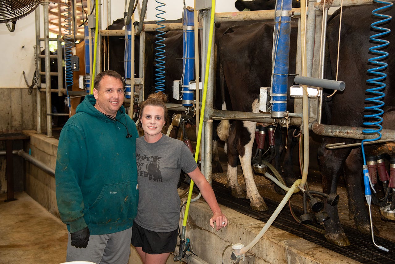 Kaleb and Erin Rodgers pose next to cows in a milking parlor