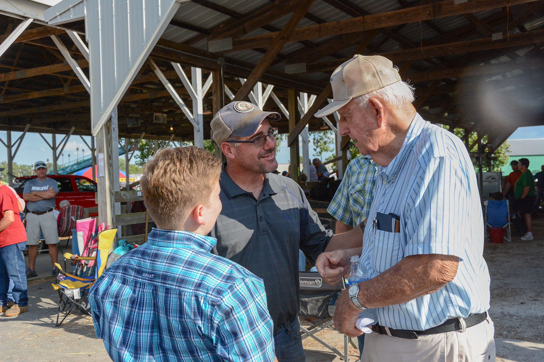 middle-aged man shakes hand of older man while young boy watches middle-aged man shakes hand of older man while young boy watches