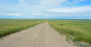 A gravel road in the middle of a prairie that disappears into the horizon
