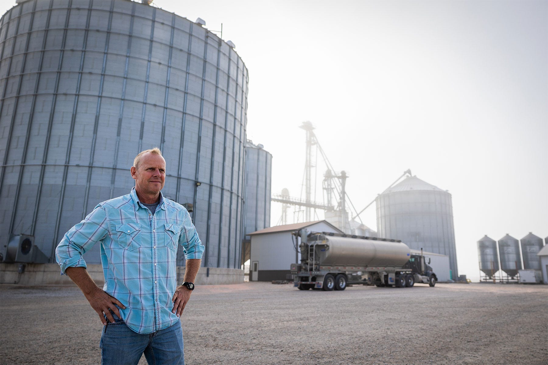 farmer standing with hands on hips in front of grain center and semitruck