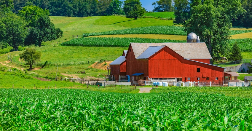 green cornfield with red barn and hills in background