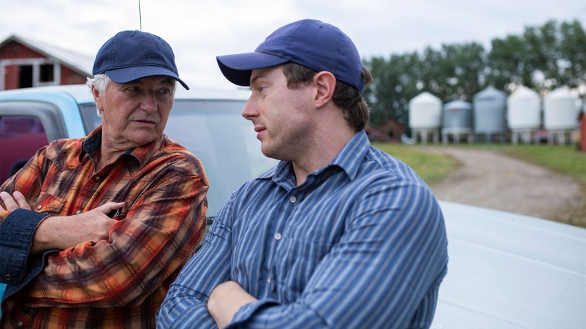  Father and son farmers talking with arms crossed on farm