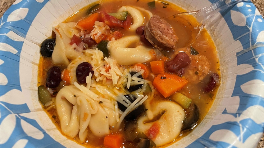  A close-up of soup with tortellini, sausage, and various vegetables