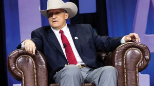 man wearing cowboy hat and suit seated in armchair 