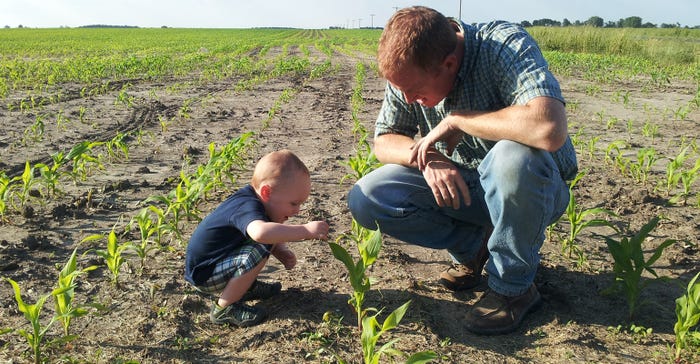 Brian Satorius and his young son kneeling in a young cornfield