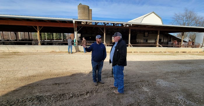 Two men standing in front of a cattle feedlot having a conversation