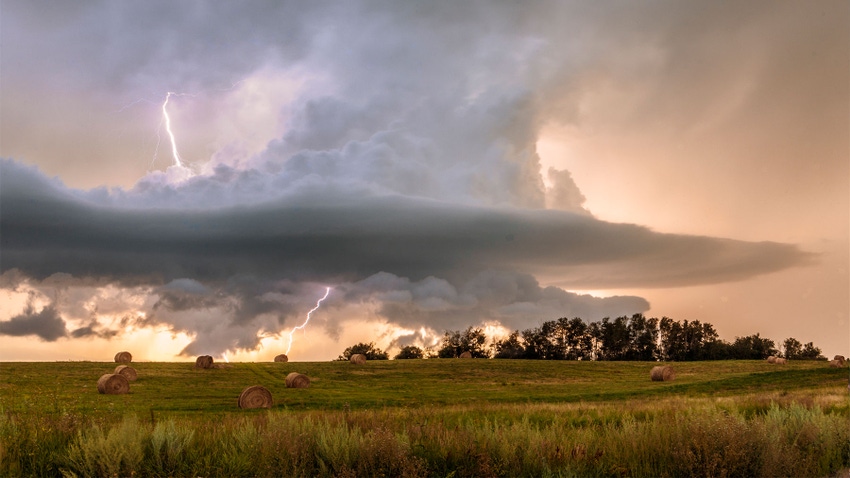 A thunderstorm over a prarie with round hay bales