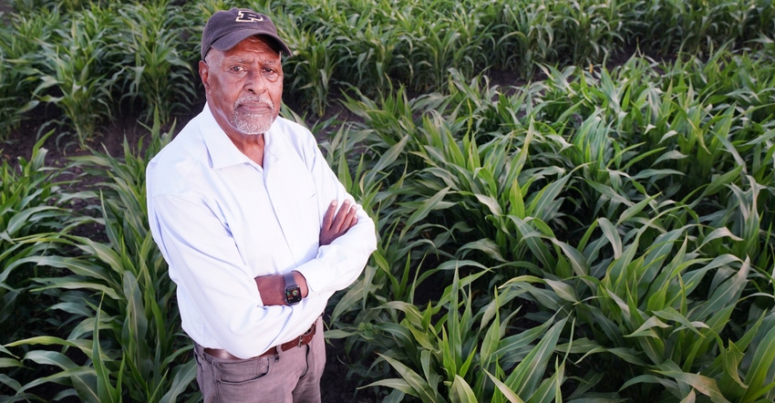 Gebisa Ejeta standing in sorghum field with arms crossed