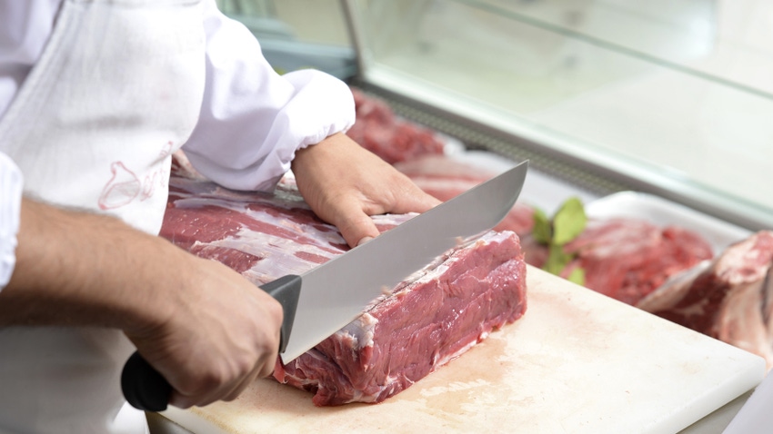 close-up of butcher's hands as he slices a chunk of beef