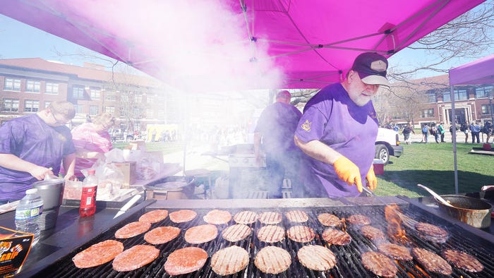 a man cooks burgers on a large grill under a tent during Purdue Ag Week q