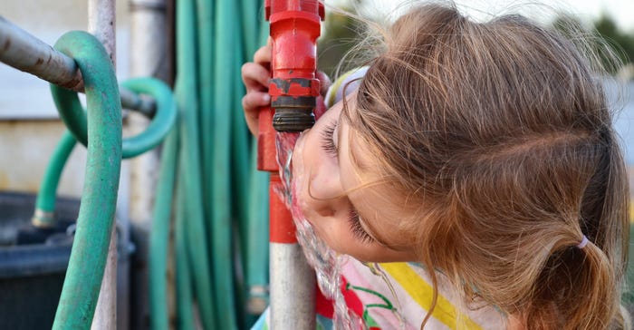 Young girl drinking from a hydrant.