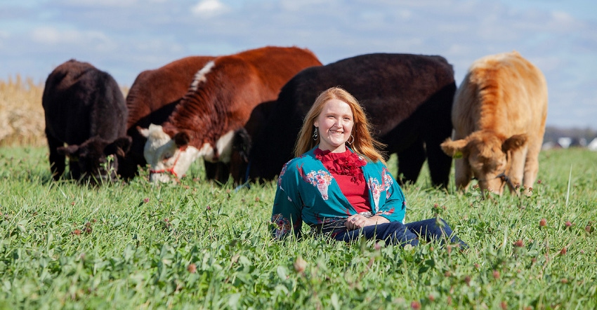 Maddy Zimmerman sitting in pasture with cows behind her