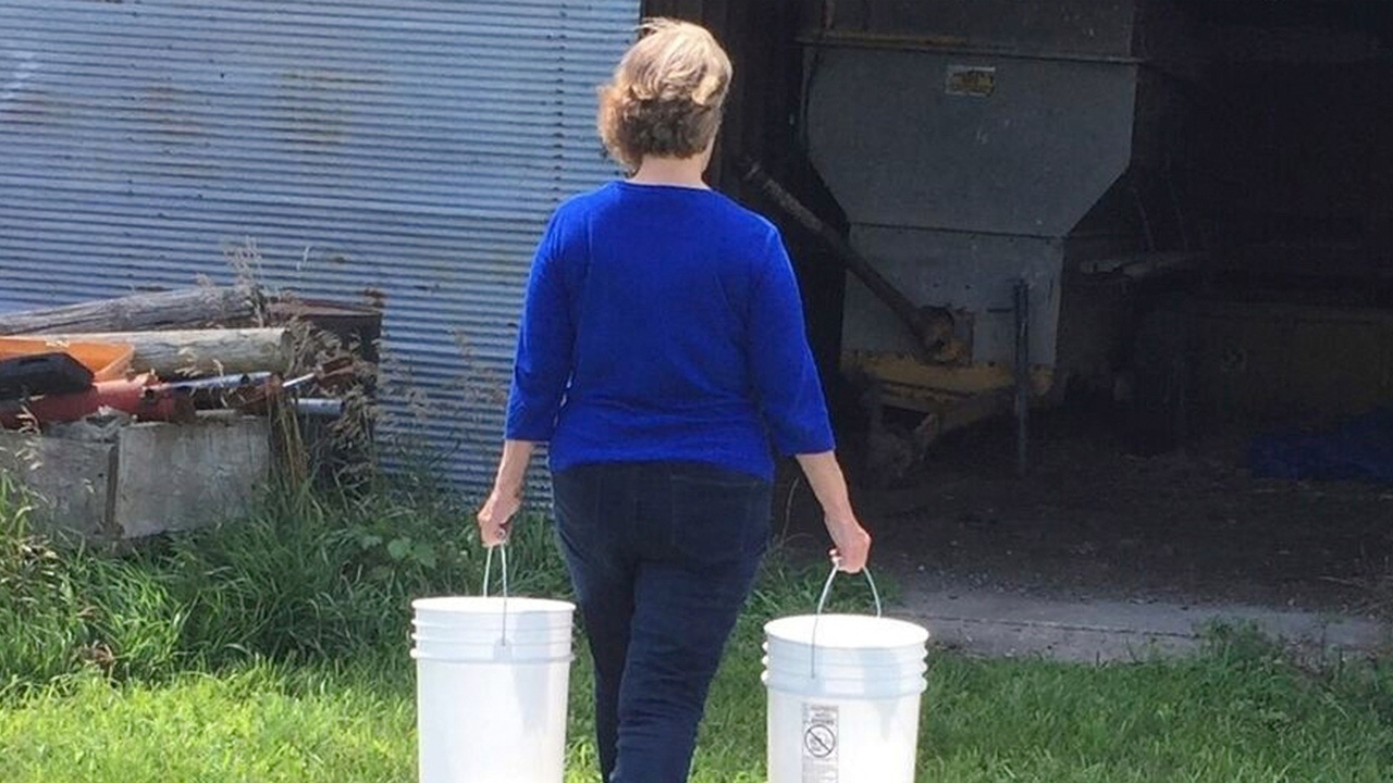 Woman with her back turned carrying two large buckets