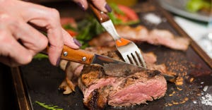 Woman hand holding knife and fork cutting grilled beef steak