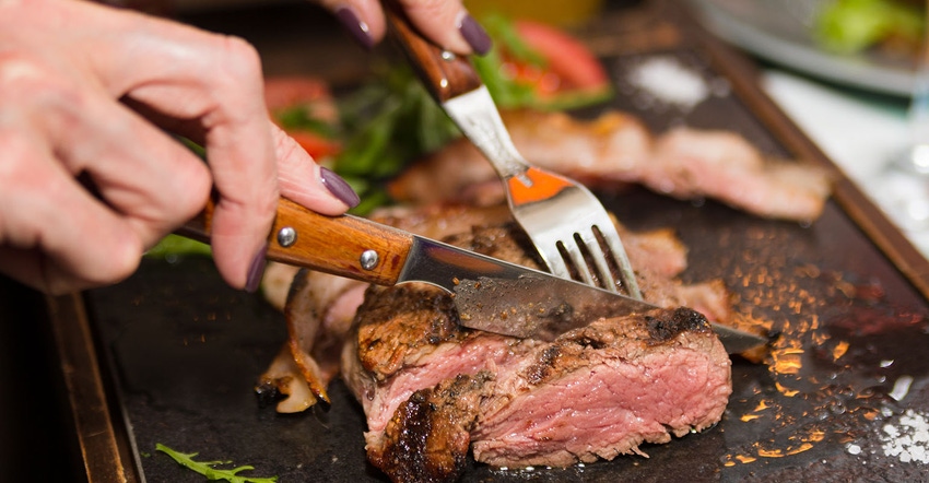 Woman hand holding knife and fork cutting grilled beef steak Woman hand holding knife and fork cutting grilled beef steak