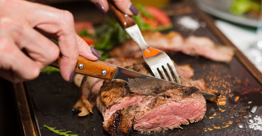 Woman hand holding knife and fork cutting grilled beef steak