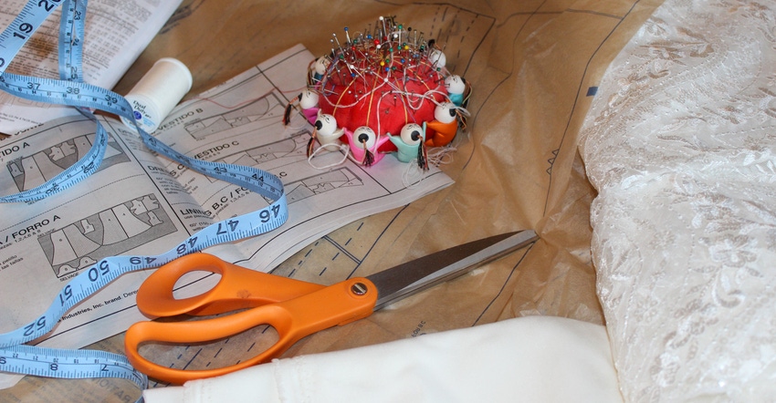 Close up shot of wedding dress fabric, sewing cushion, measuring tape, and scissors