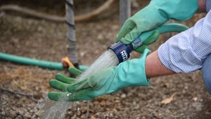 A hand with gloves holding a hose with running water