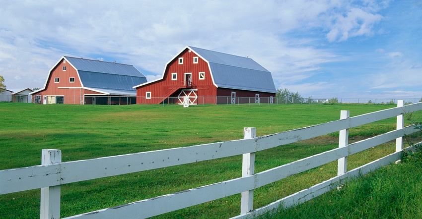 Red barn with a white wooden fence on the pasture perimeter