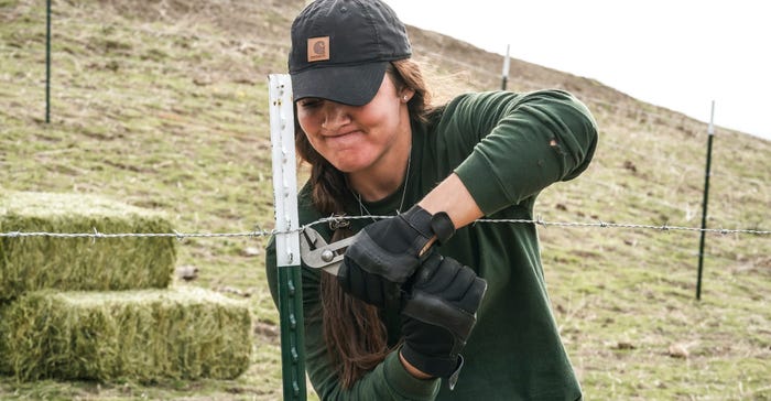 Melissa Burns working with pliers on a barbed wire fence