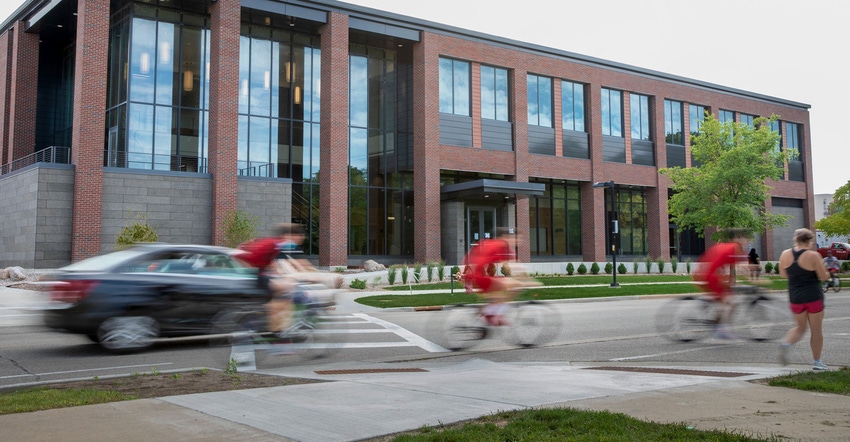 A brick and glass building and a motion blur of cars and people on bicycles quickly passing by