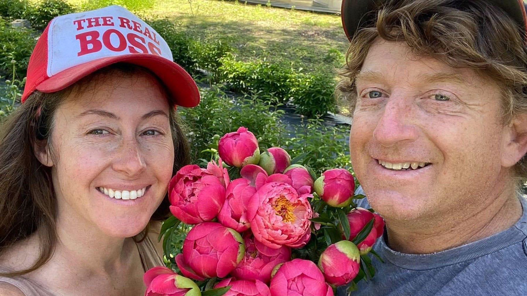 Woman and man holding bouquet of hot pink peonies.