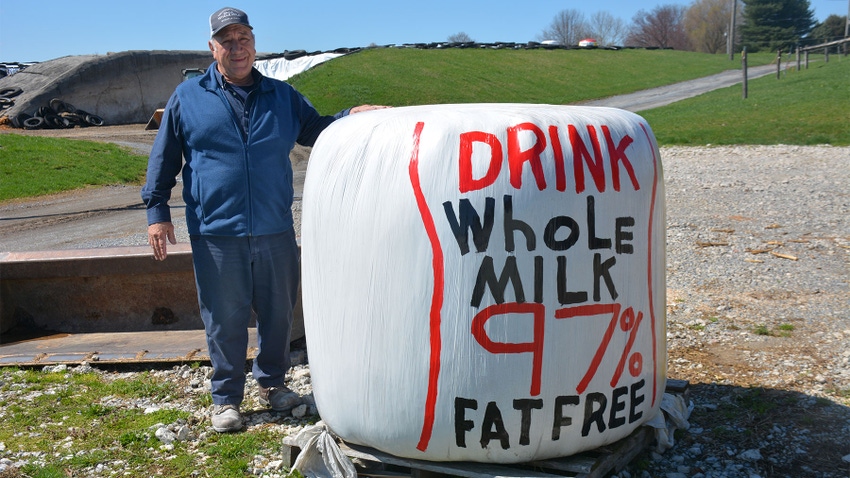 Dairy farmer Nelson Troutman stands next to a plastic wrapped bale of hay that has the words "Drink whole milk 97 percent fat free"