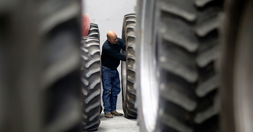 Framed by tractor tires, a mature farmer works on his equipment.