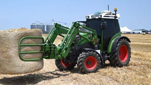 A green tractor moving a hay bale
