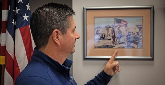 Jerry Costello pointing to photo hanging on the wall that was taken while he was overseas serving during the Gulf War