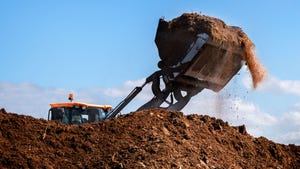 Excavator shovel working on large heap of fertilizer