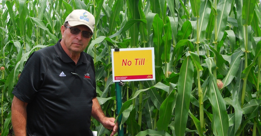 Bill Drury, a Wright County farmer standing infront of cornfield with No Till sign