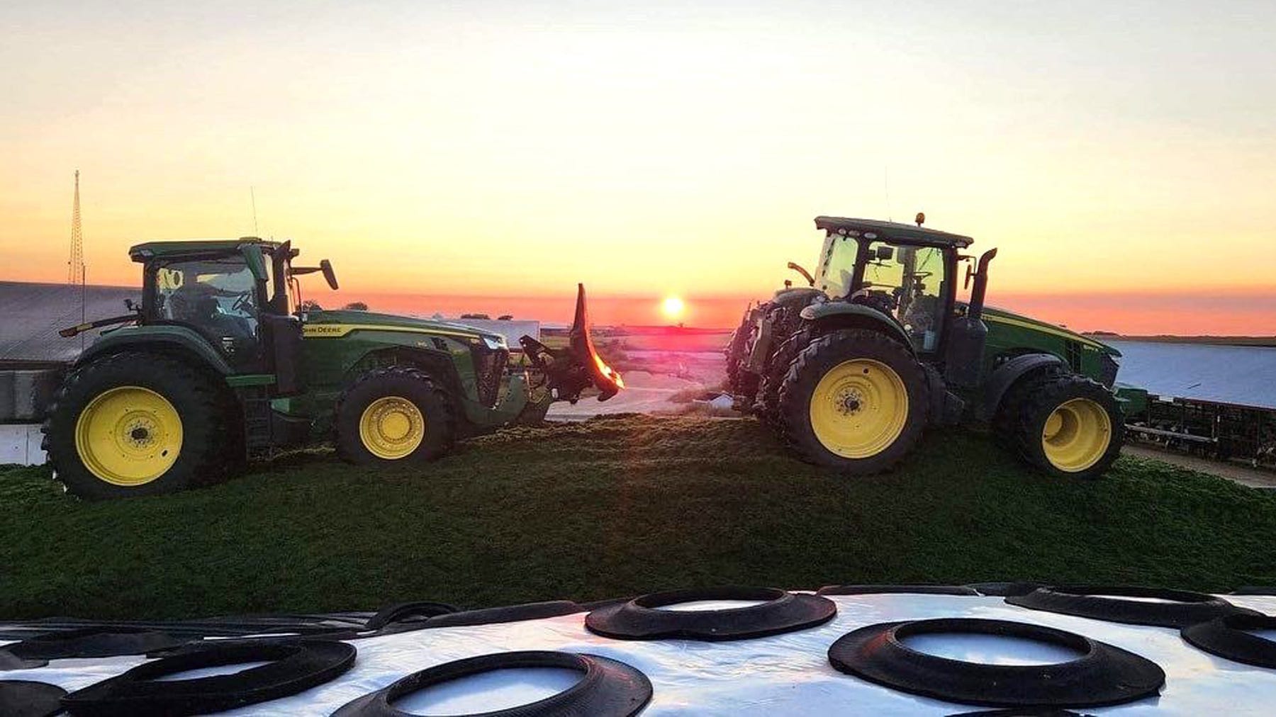 A pair of tractors pack haylage in a bunker silo at sunset
