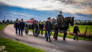 Indiana National Guard Caisson Platoon members leading a funeral procession with horses pulling a casket in a wagon