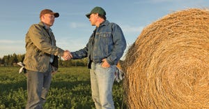 two farmers shaking hands next to round bale