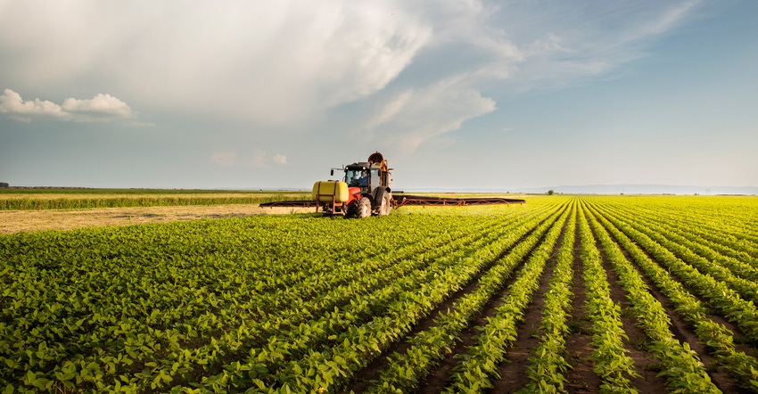 Tractor spraying pesticides on soy field