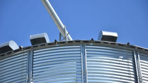 The top of a metal grain bin against a blue sky