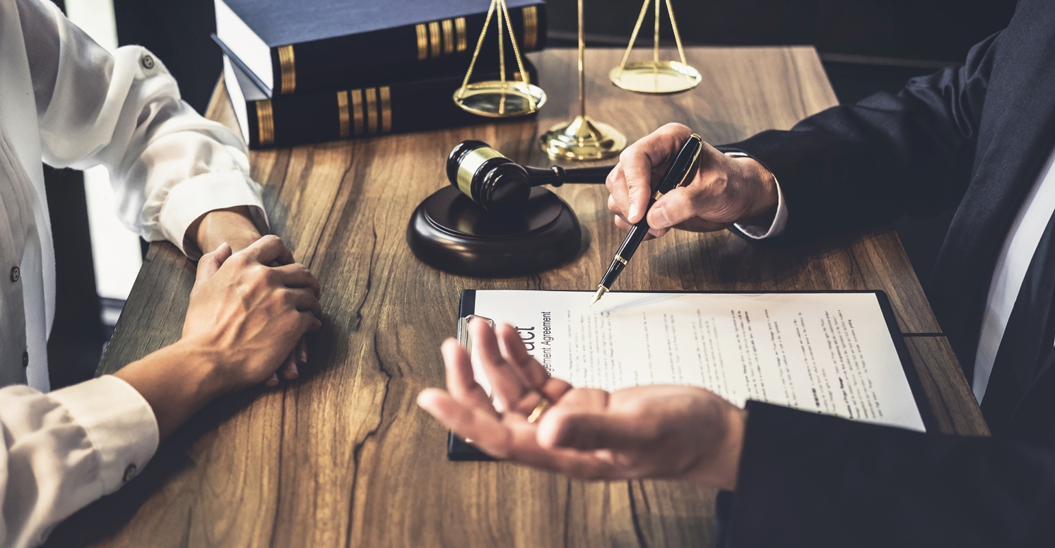 Lawyer discussing legal documents with a client in a law office, with a gavel and scales of justice in the background, illustrating the contesting a will process.