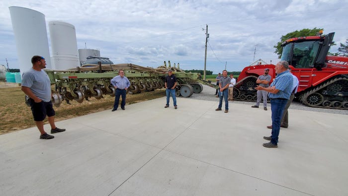 A group of men standing around and talking on a cement patio next to tractors and farming equipment