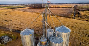 Aerial view of grain bins on Midwest farm at dusk with USA flag atop grain leg