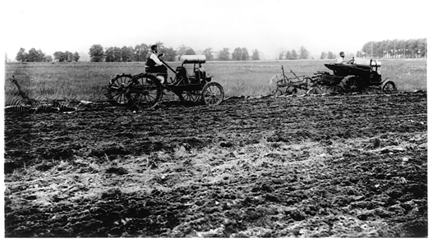 A scan of a vintage black and white photograph of two farmers plowing a field with Model T cars