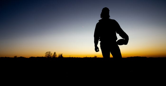 silhouette of man holding football on hip as sun sets in background
