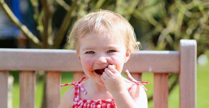 Little girl eating grilled meat outdoors