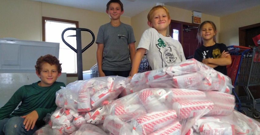A group of kids smiling and standing around a pallet of packaged hamburger meat
