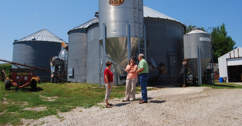 two woman and a man talking in front of grain bins