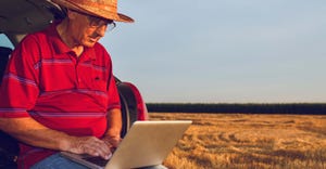 Farmer examining income on laptop after the harvesting of wheat.