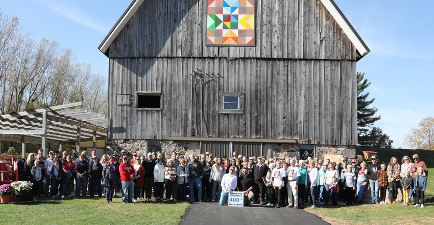 Large group of people in front of barn with quilt painting hanging on it
